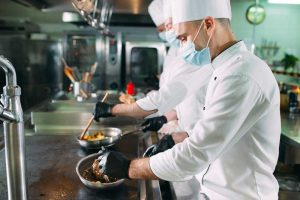 Masked chefs prepare food in commercial kitchen